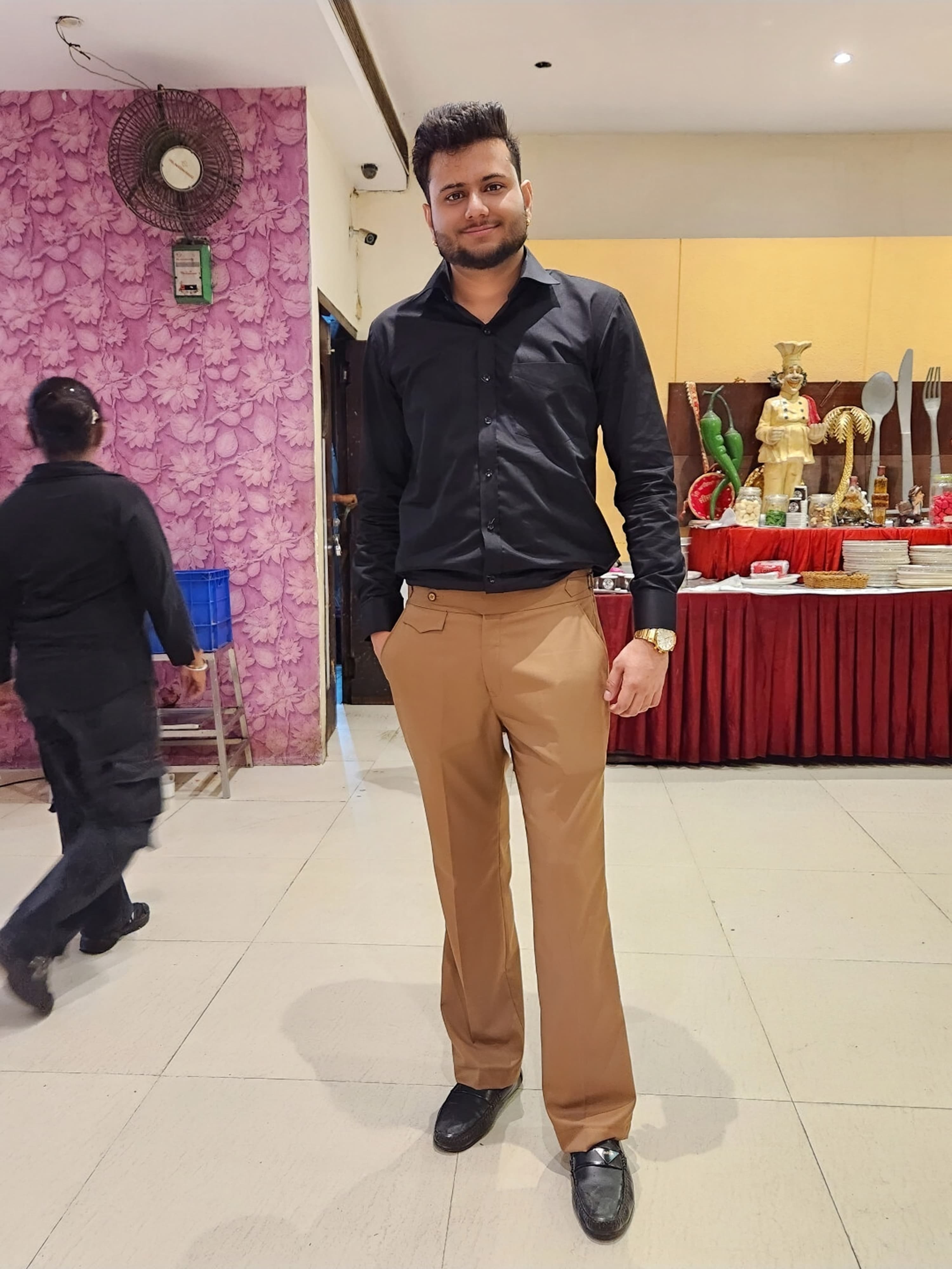 Shubham Verma in a black shirt and tan trousers, standing in a banquet hall