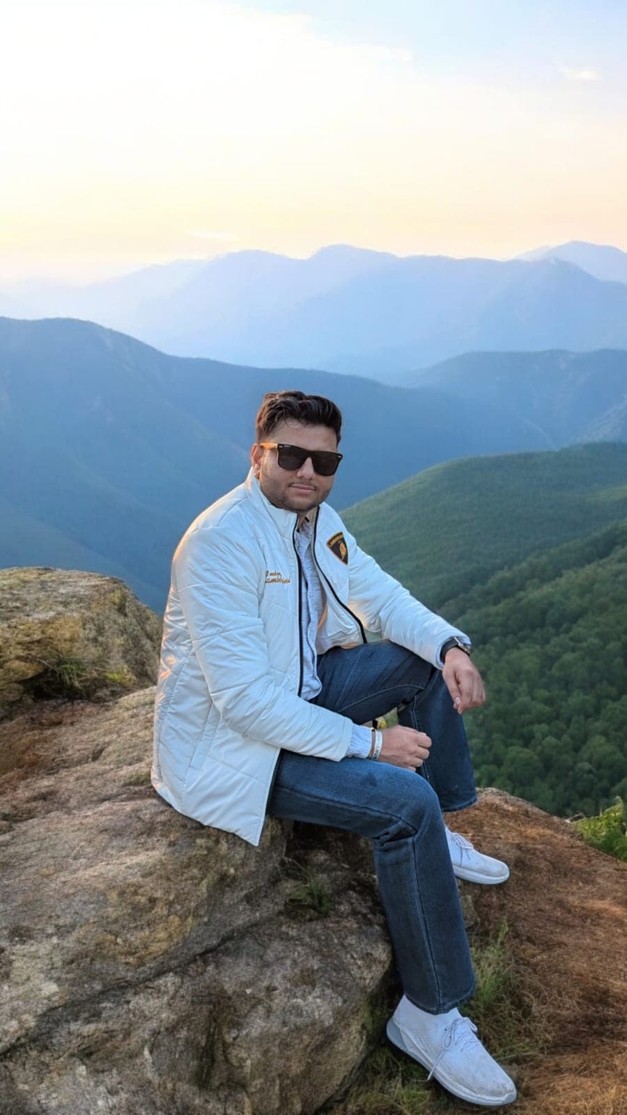 Shubham Verma sitting on a rocky peak overlooking mountains at sunset